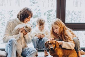 Mother with son and daughter playing with their dog at home by the window